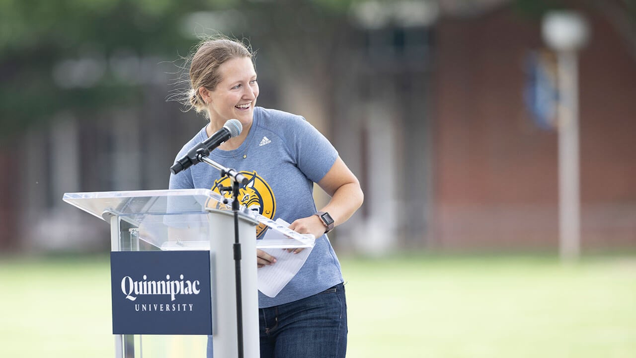 QU alumna and NHL Boston Bruins hockey operations staff Danielle Marmer speaks to new students from a podium