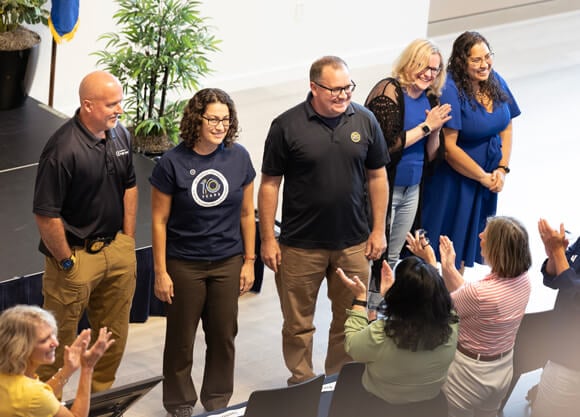 The 2025 Center for Excellence Honorees smile as colleagues clap and cheer around them