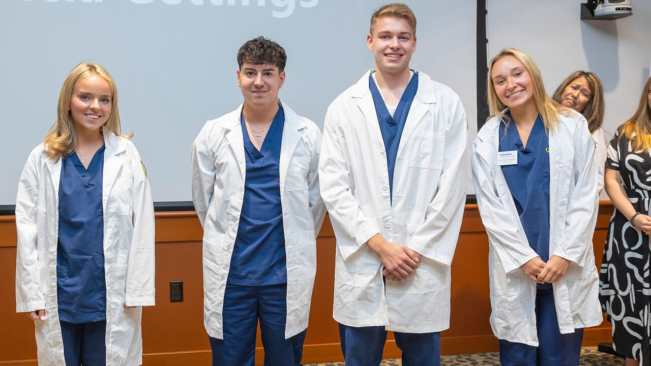 four nursing students smile in their white coats