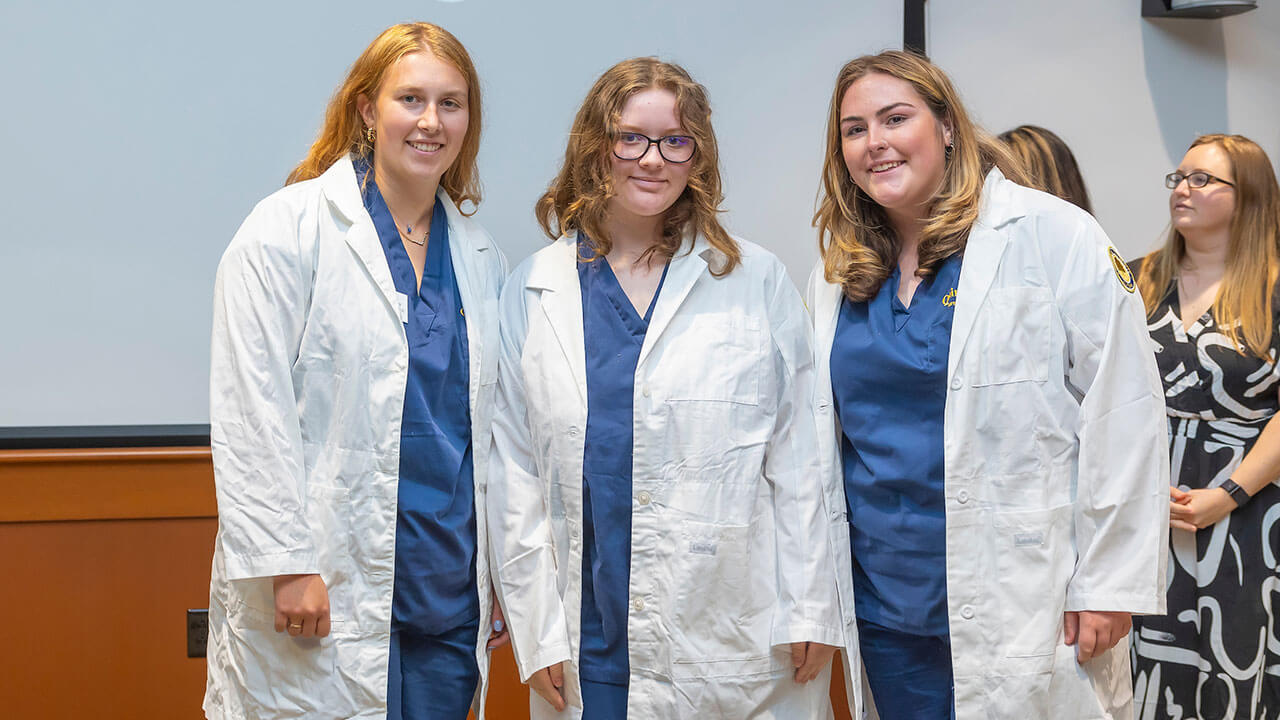 three nursing students smile in their white coats