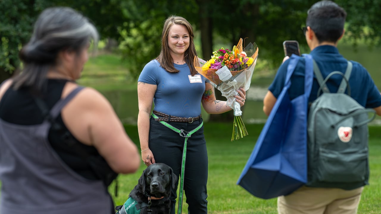 Individual holds flowers while a dog sits next to them