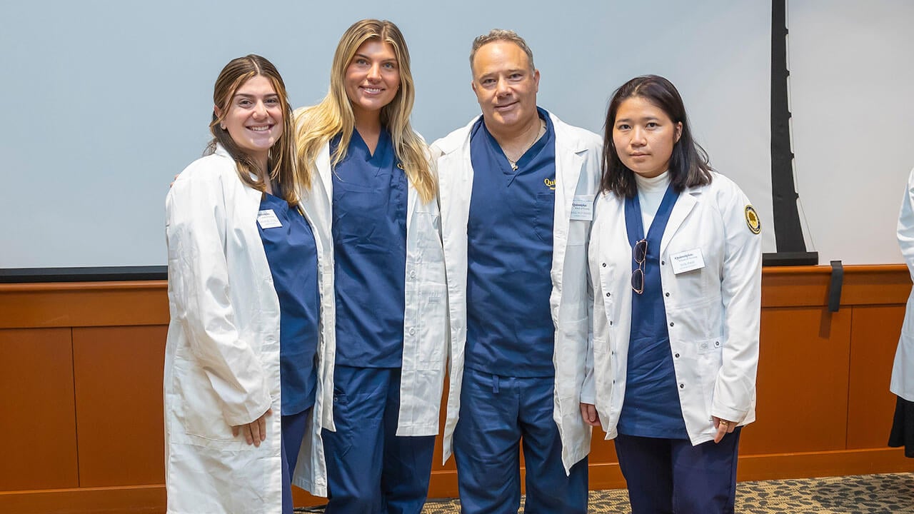 four nursing students in white coats smile for their photo to be taken