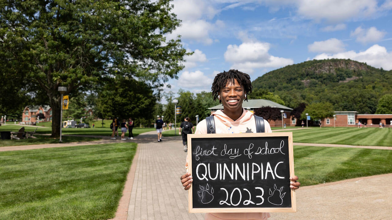 Student smiles on the Quad holding a sign