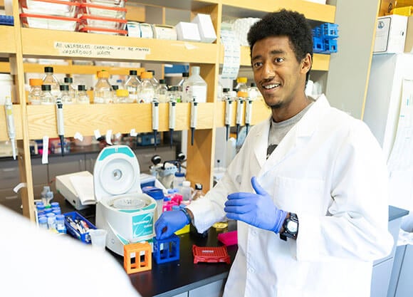 Dagmawi Bogale wears a lab coat and works with lab equipment