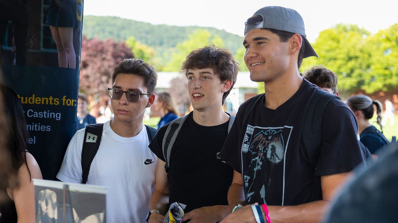 Three students visit a club table on the Quad to learn more