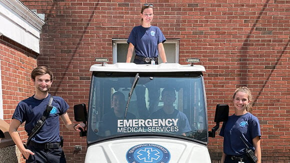 QU EMS Members, Charles Dunn, Vanessa Infante and Heidi Reinemann standing outside of their Club Car.