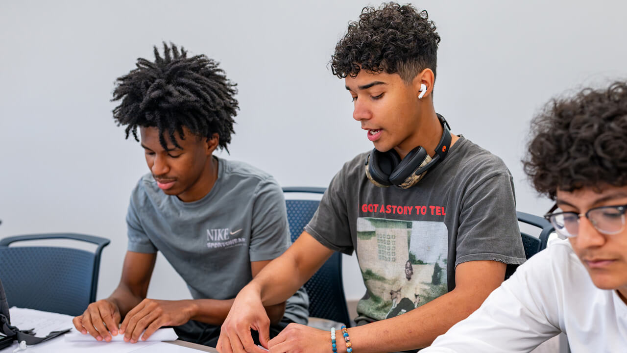 Three male students folding pieces of paper.