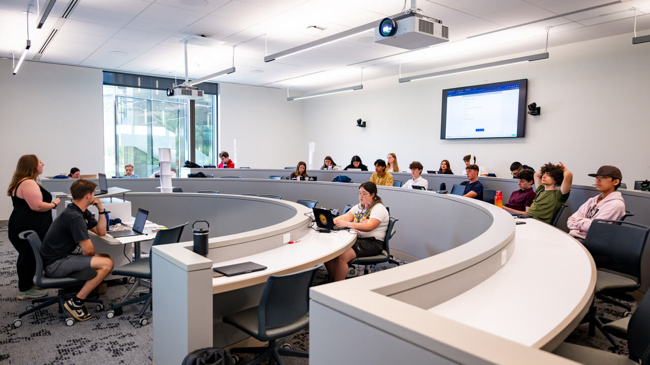 A shot of the classroom with students sitting at curved desks.