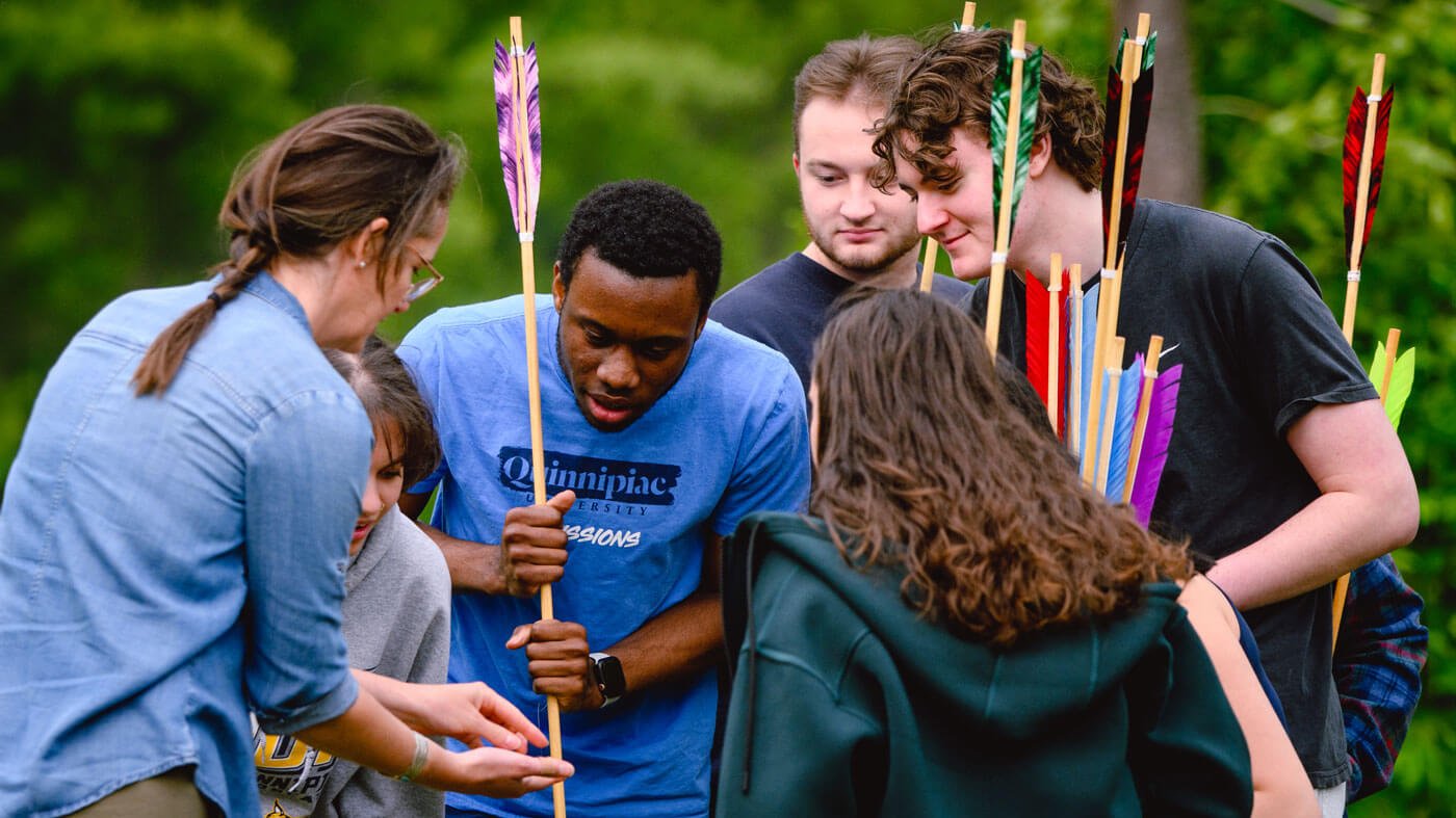 Students observe an ancient artifact during a spear throwing activity.