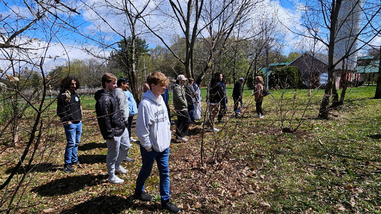 A group of students walking through woods next to a barn and silo.