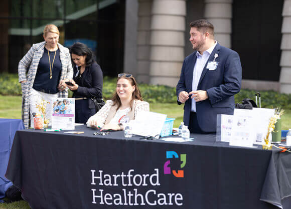 Two Hartford HealthCare employees staff a table at an outdoor wellness fair