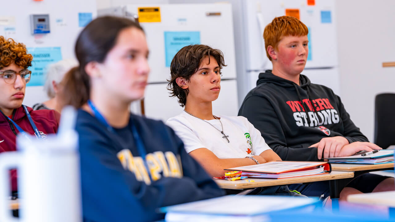 Four students sitting at a desk looking at the front of the room.