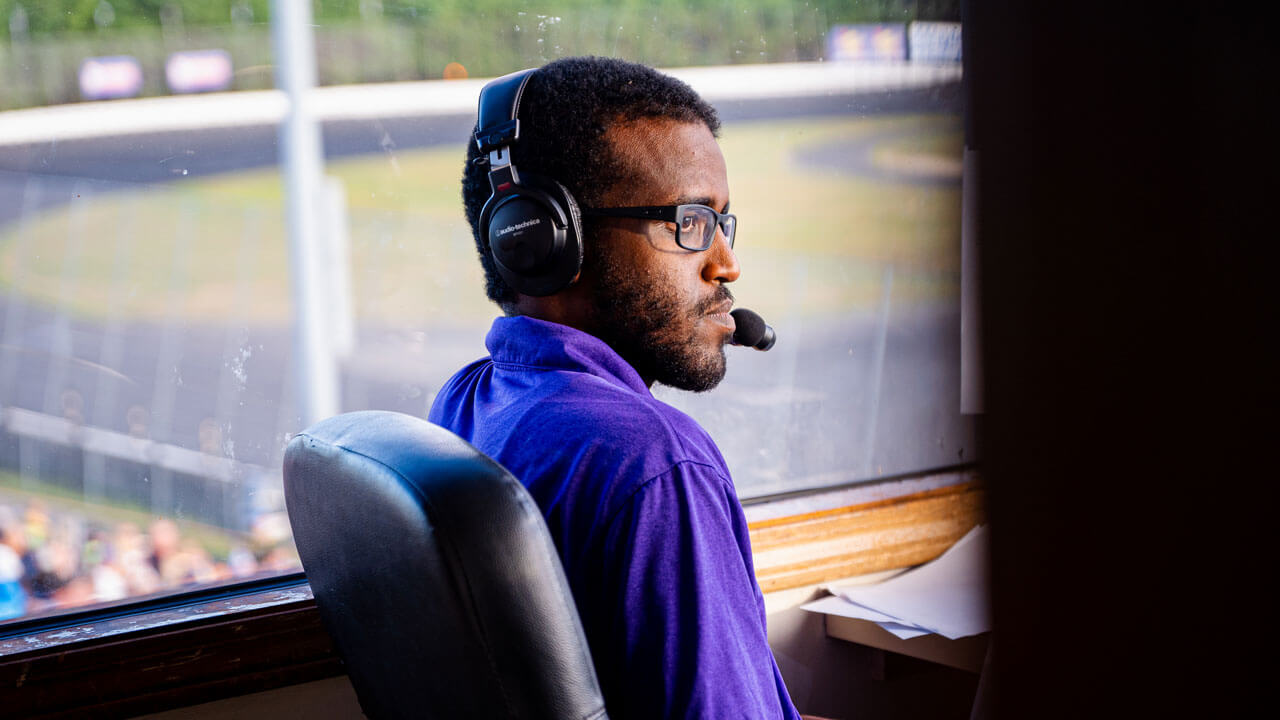 Bonssa Tufa sitting at a desk with a headset on, with a race track in the background