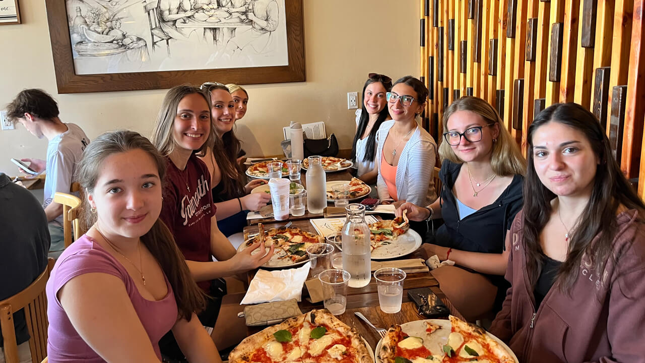Eight female students sitting around a table with their pizzas.