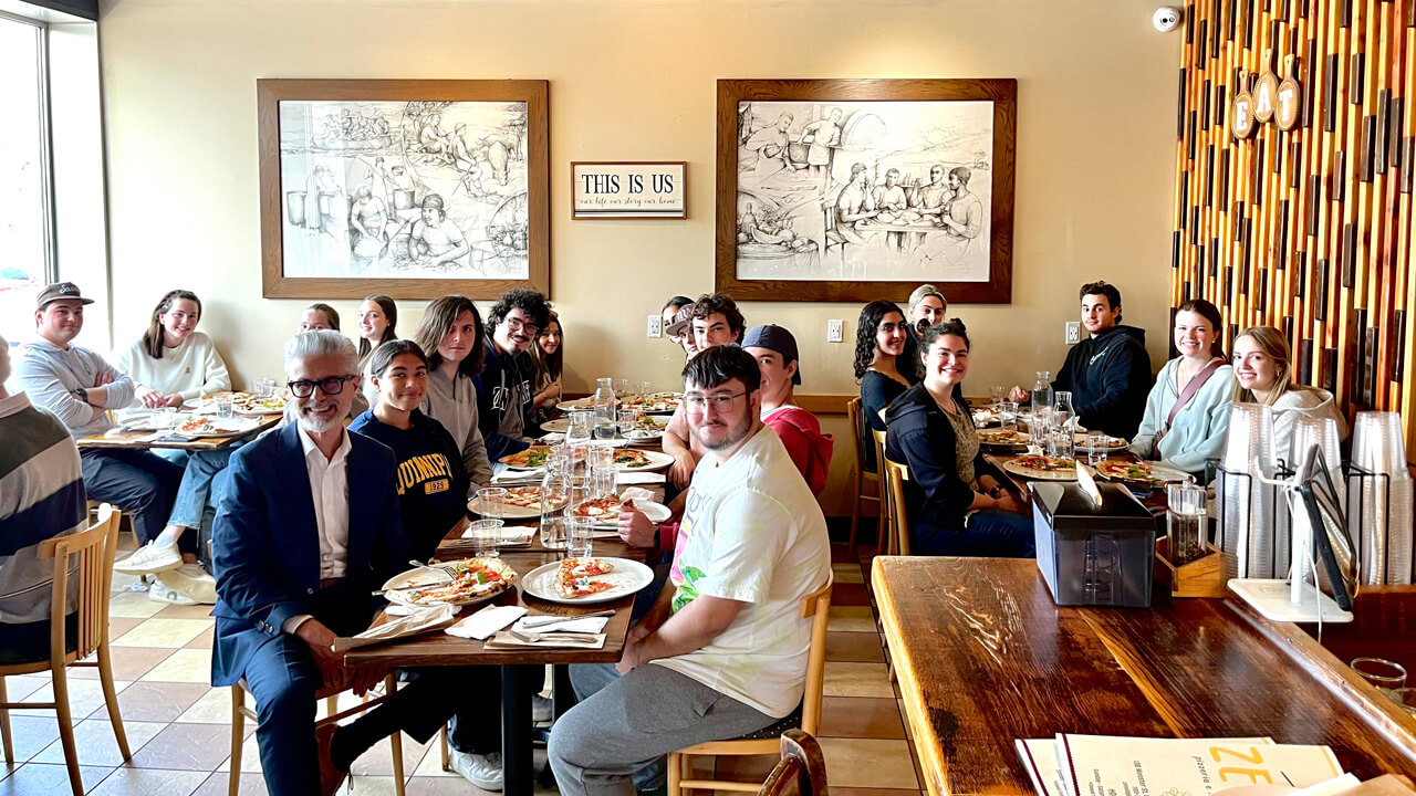 A shot of the interior of the restaurant with Professor Naitana and the participating students smiling at their tables.