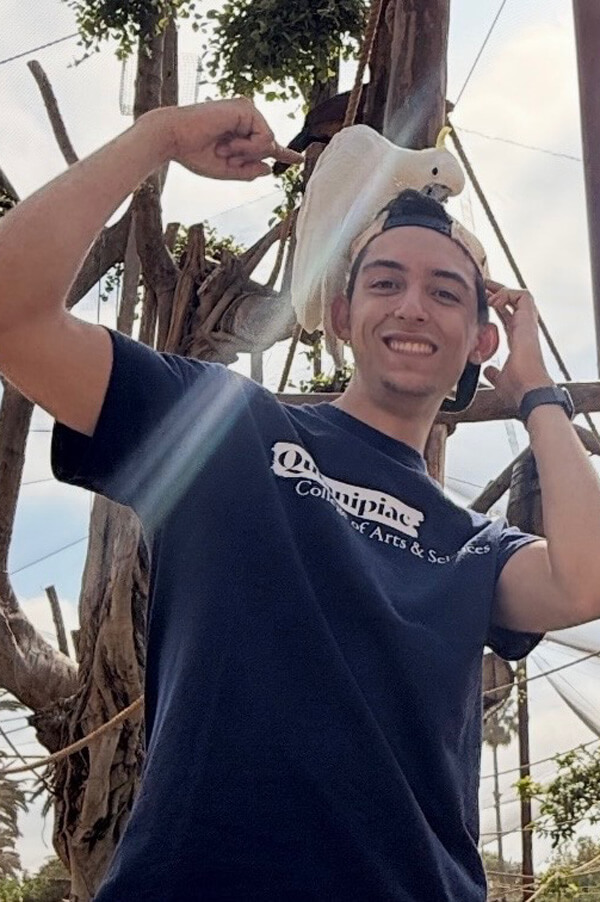 Photo of Younes Benbrahim smiling with a white bird perched on his head.