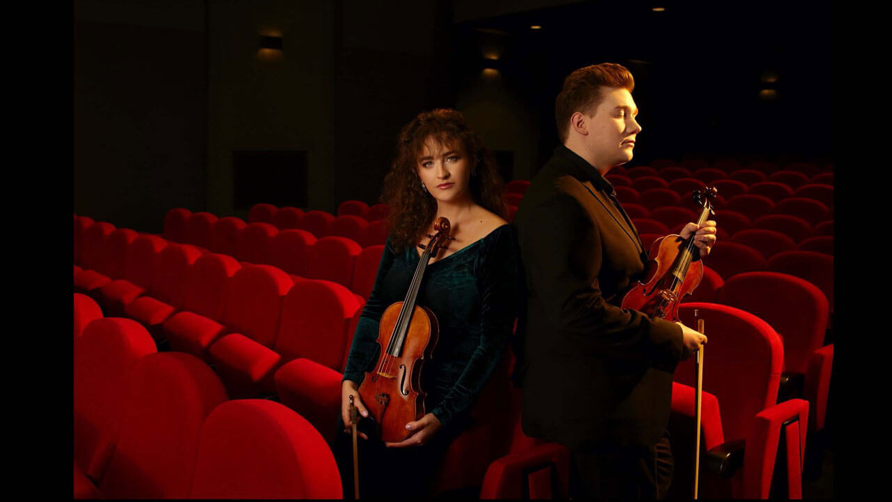 Marta Gidaszewska and Robert Aguniak in a theater holding violins