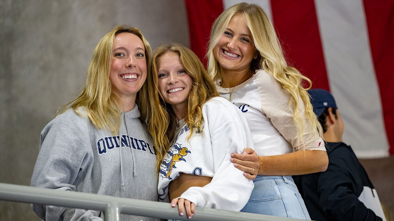 Three students take a photo at the banner raising ceremony