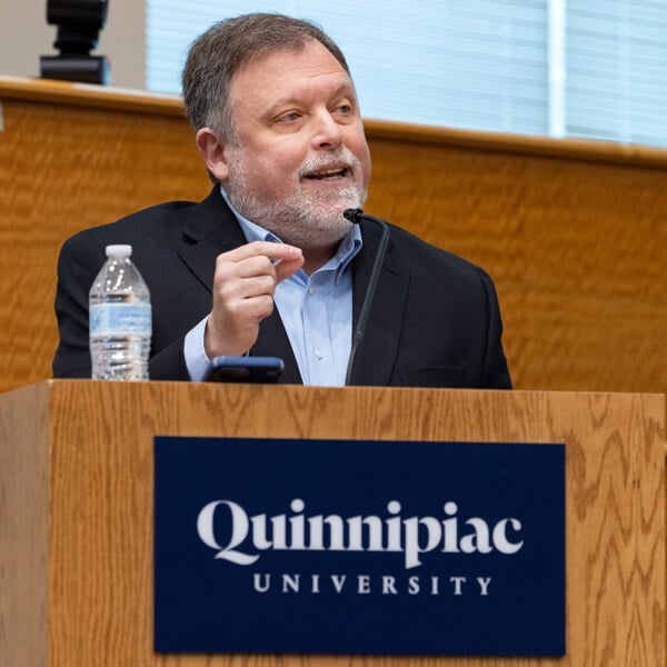 Tim Wise gestures with his hand as he speaks behind a Quinnipiac podium