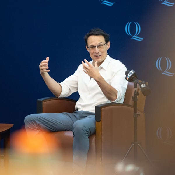 Steve Kornacki sits in a leather armchair and speaks to a crowd in the Quinnipiac Mount Carmel Auditorium