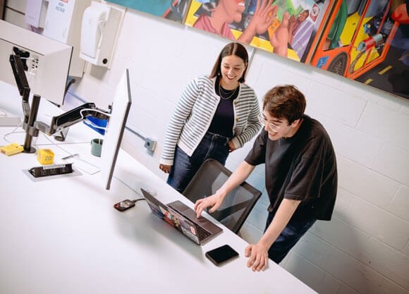 a male and female bending over, looking at a laptop