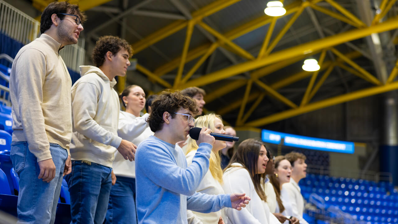 Members of The Legends a cappella group wear white and sing in the stands