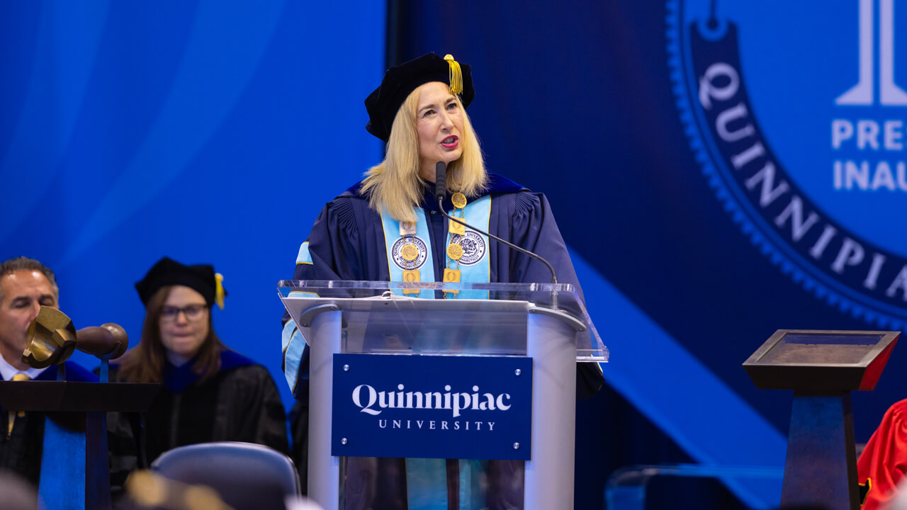 Marie Hardin in academic robes speaks at a Quinnipiac podium during her Inauguration