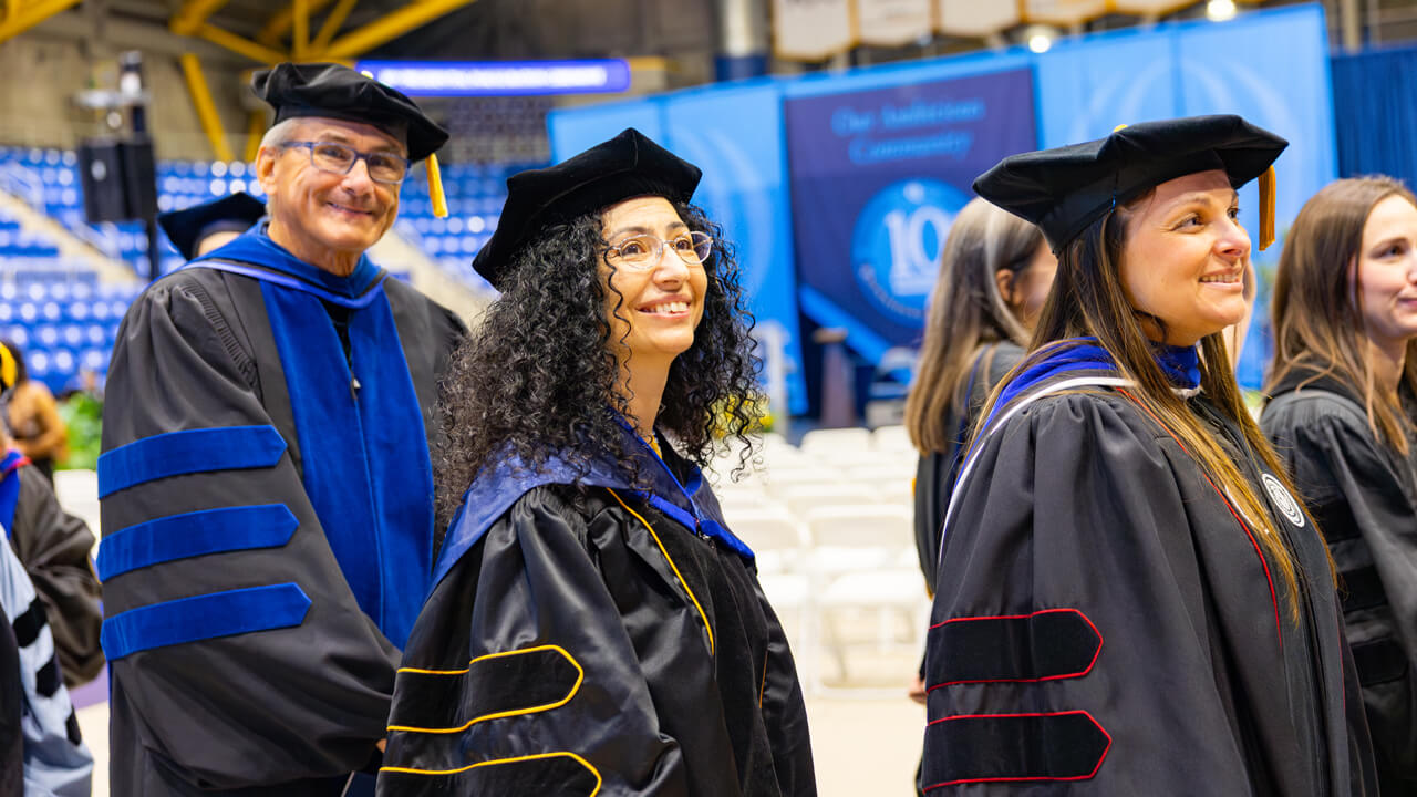 Several faculty members smile as they process through the arena