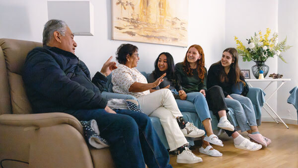 3 female students talking to an elderly couple, all sitting on a couch