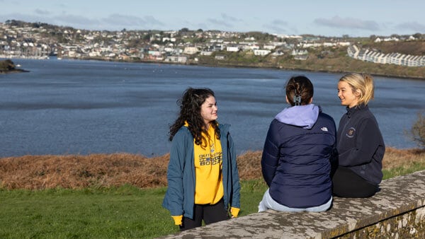 3 students sitting outside looking at a lake