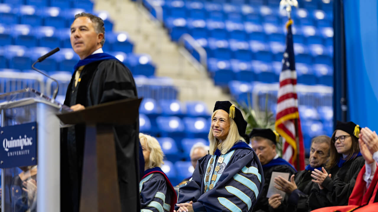 Chuck Saia delivers remarks from the podium as Marie Hardin and administrators look on