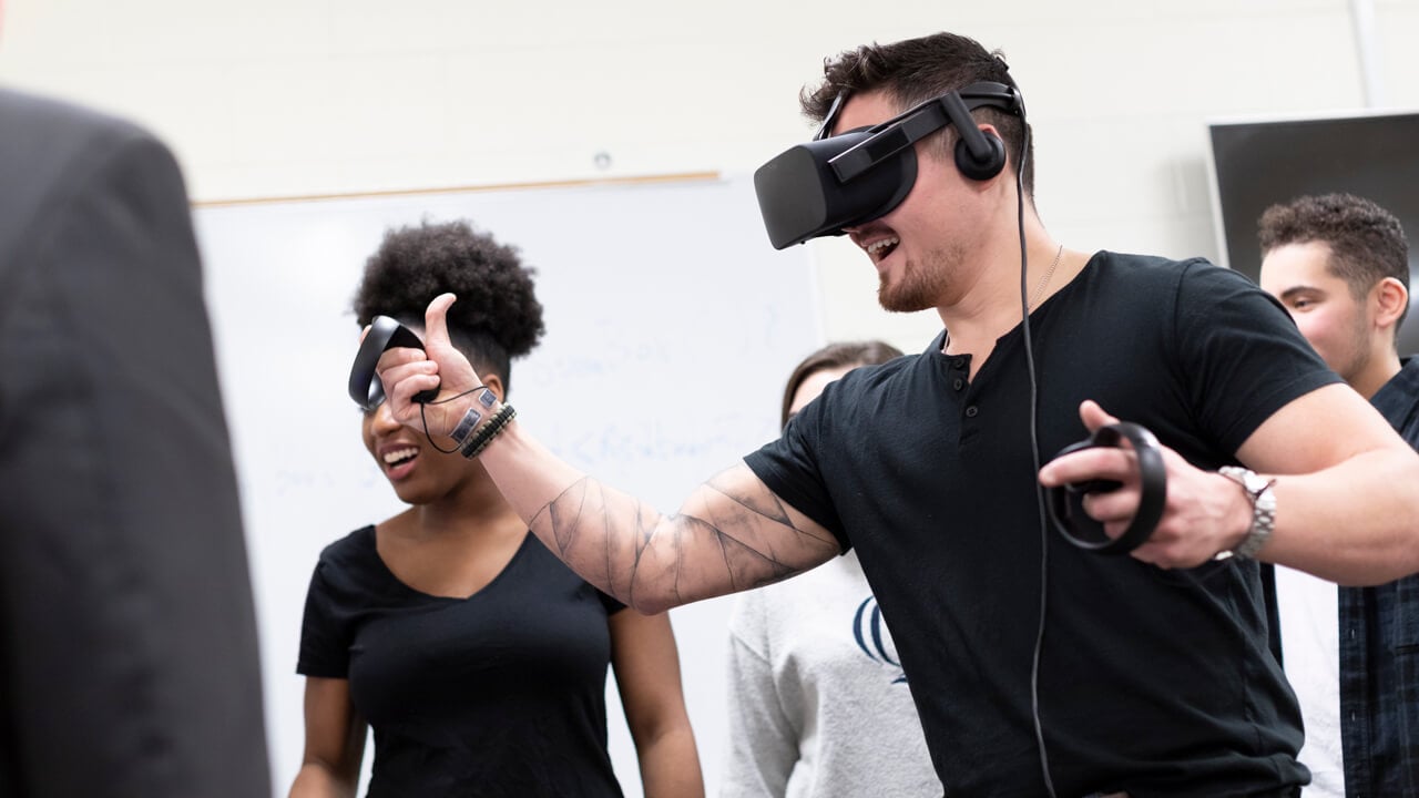 A student wearing a VR headset moves hand controllers