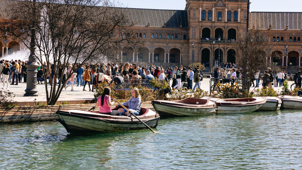 2 students in a rowboat with a large crowd in the background in Spain