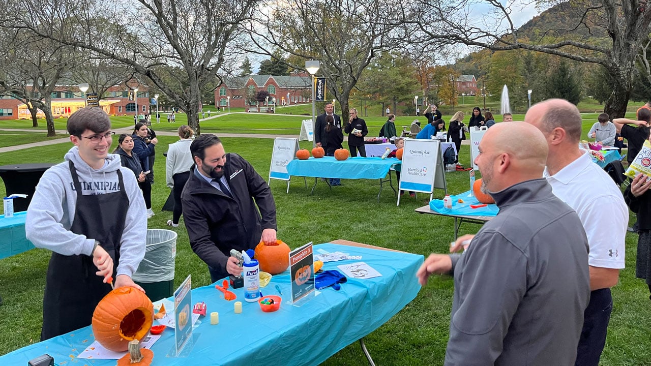 Group smiling and talking while they carve pumpkins outside on the lawn