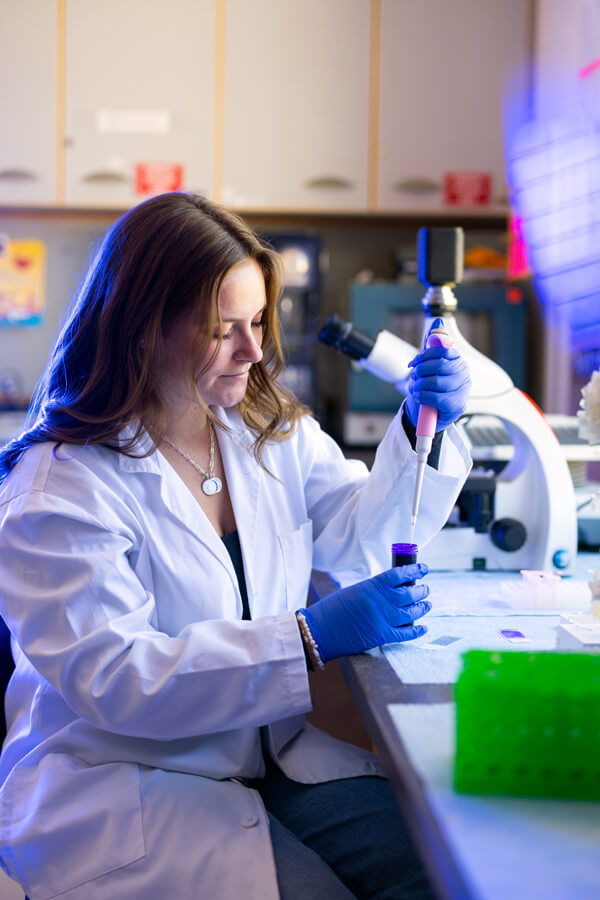 Nikki Syme uses a dropper while conducting scientific research in a lab.