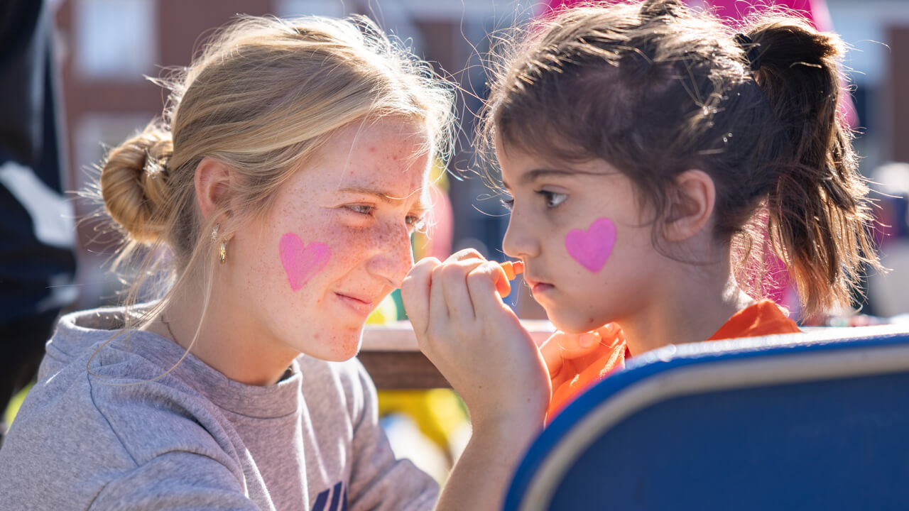 Person paints pink hearts onto another persons face