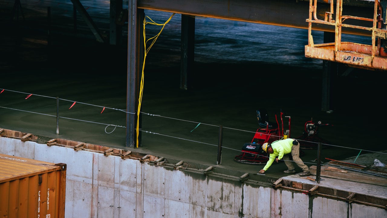 A wide view of the south quad construction with a man in a bright sweatshirt and hat working.