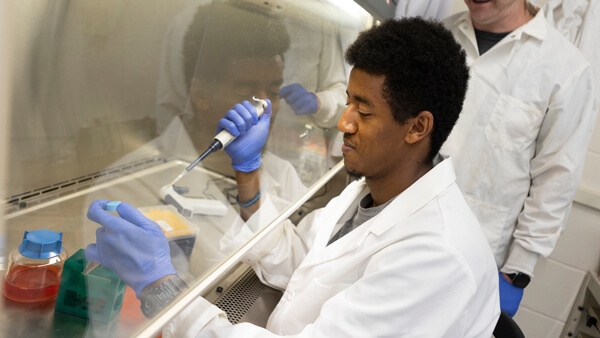 An international student in a lab code performs an experiment with a faculty member