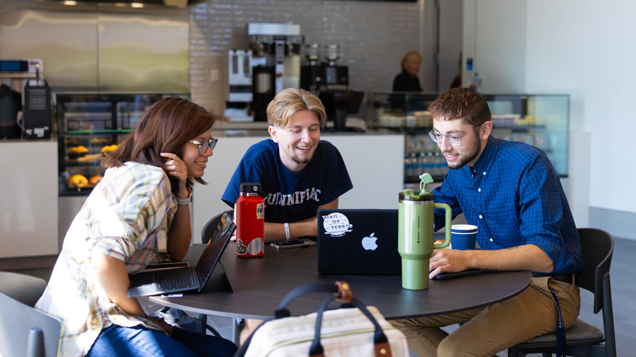 3 students working together at a table with their laptops at the School of Business Cafe