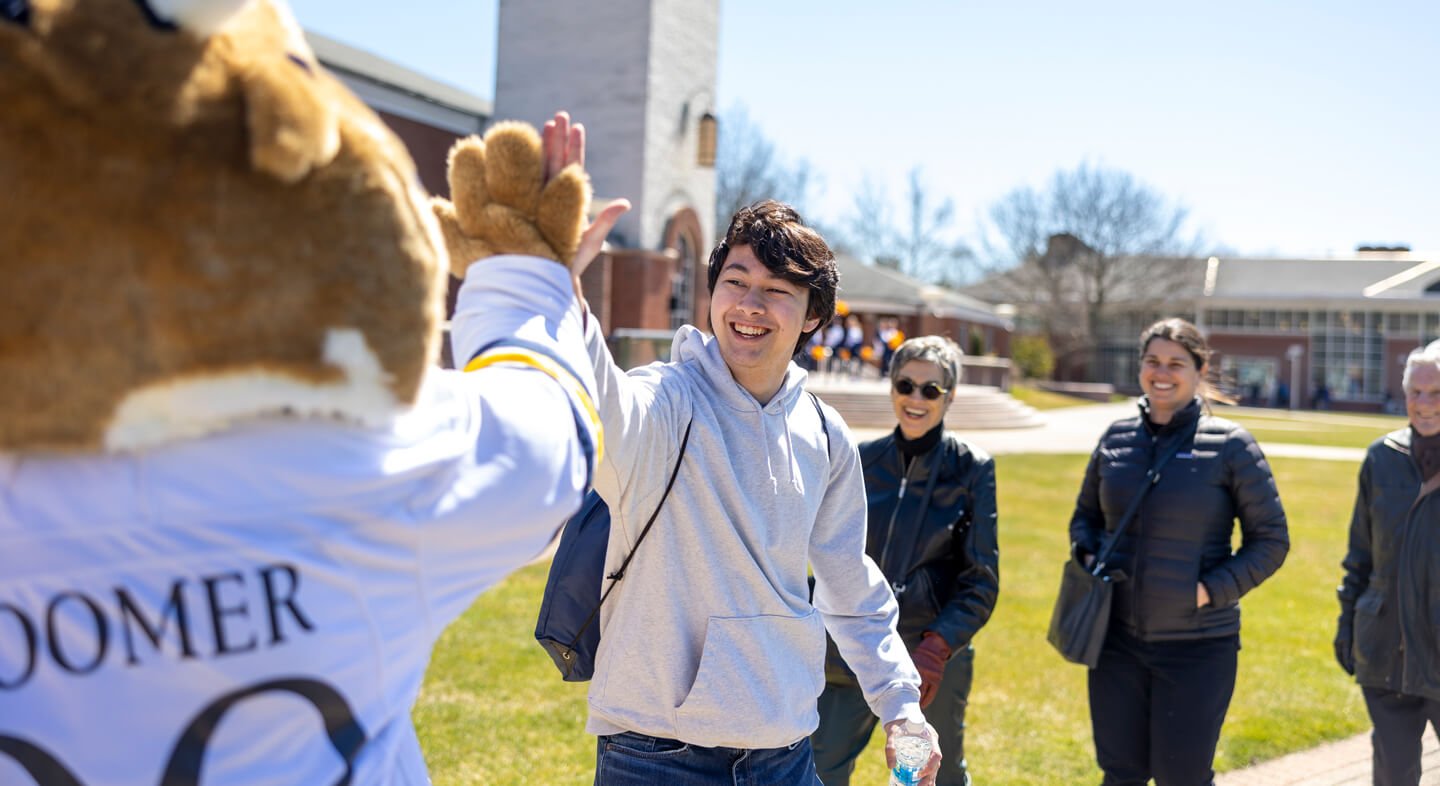 An admitted student high fives Boomer the mascot on the quad while his family smiles behind him