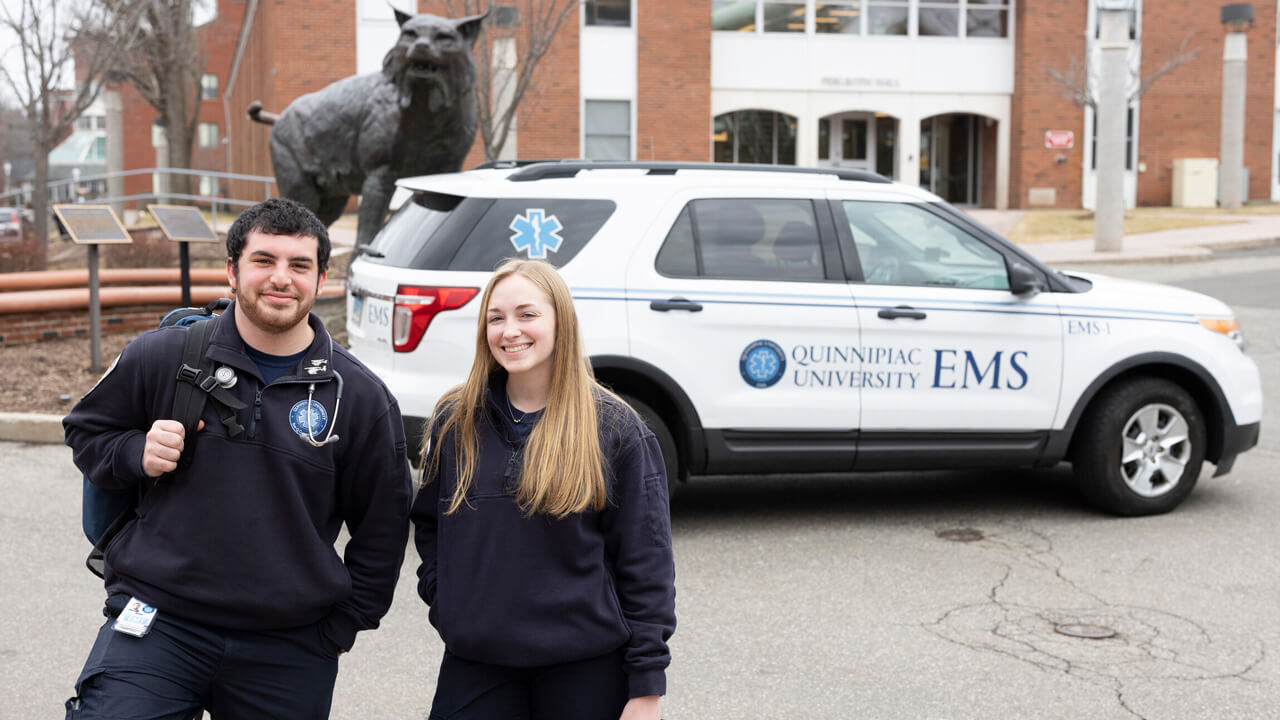 Quinnipiac University EMS students Abby Crowell and Alex Bayer standing in front of the QU EMS SUV