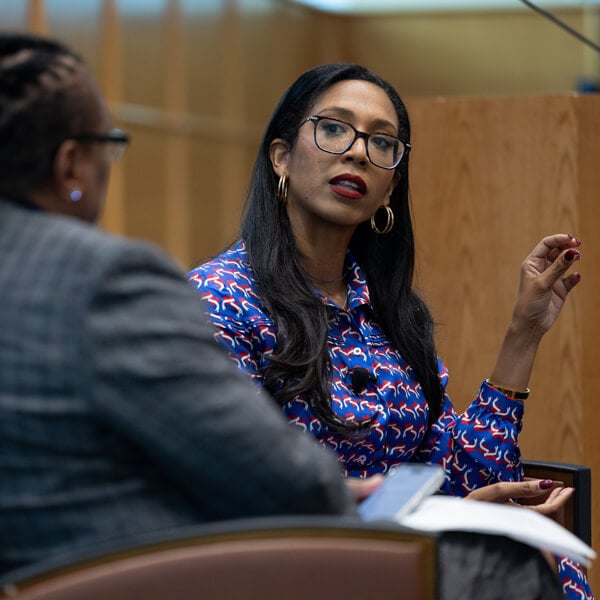 Leah Wright Rigueur seated in an arm chair speaks with a staff member in the Quinnipiac auditorium