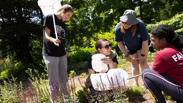 Student holds net as other students inspect plants