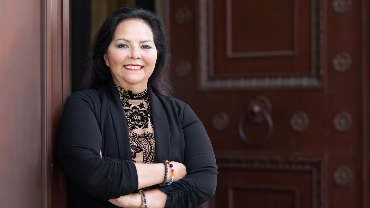 Margaret Castinado, JD '98, stands with her arms folded and smiles into the camera.