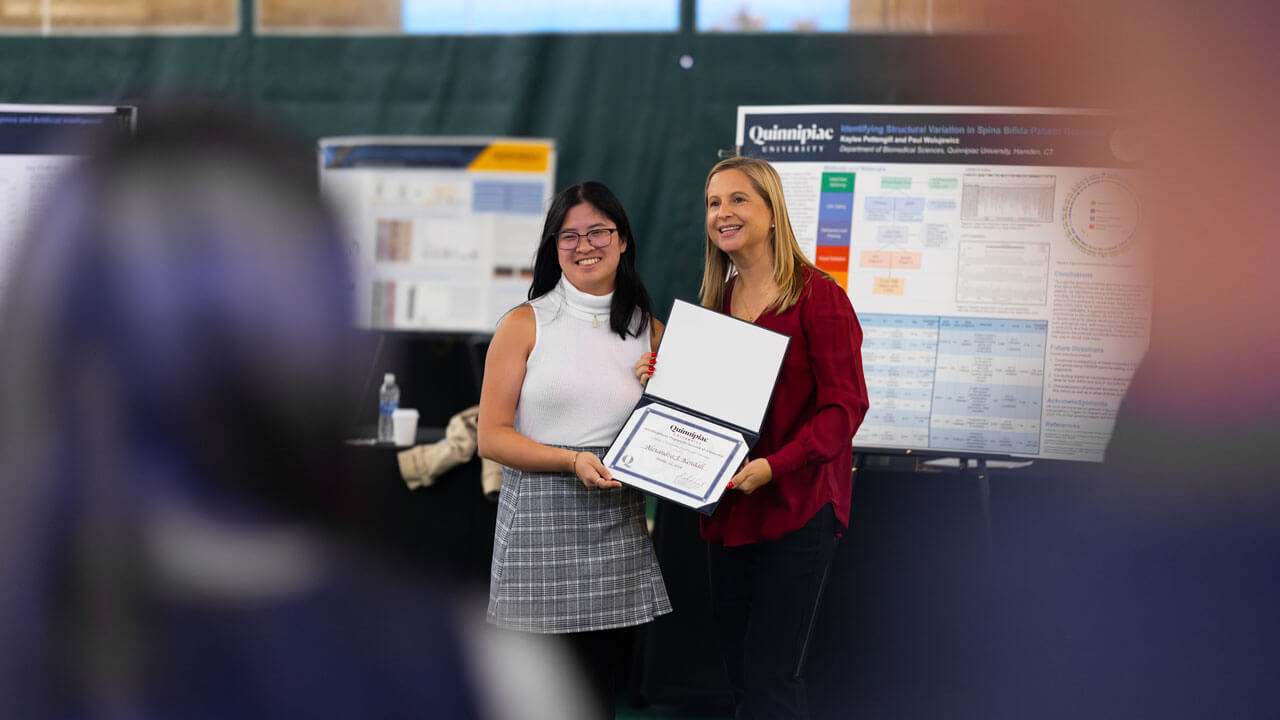 Professor of public relations Katie Place smiles alongside a student, while both of them hold an award