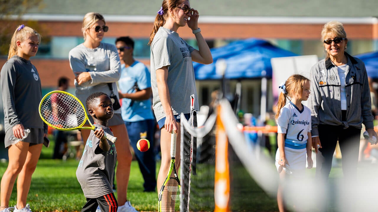 Little boy playing tennis with the Quinnipiac tennis team