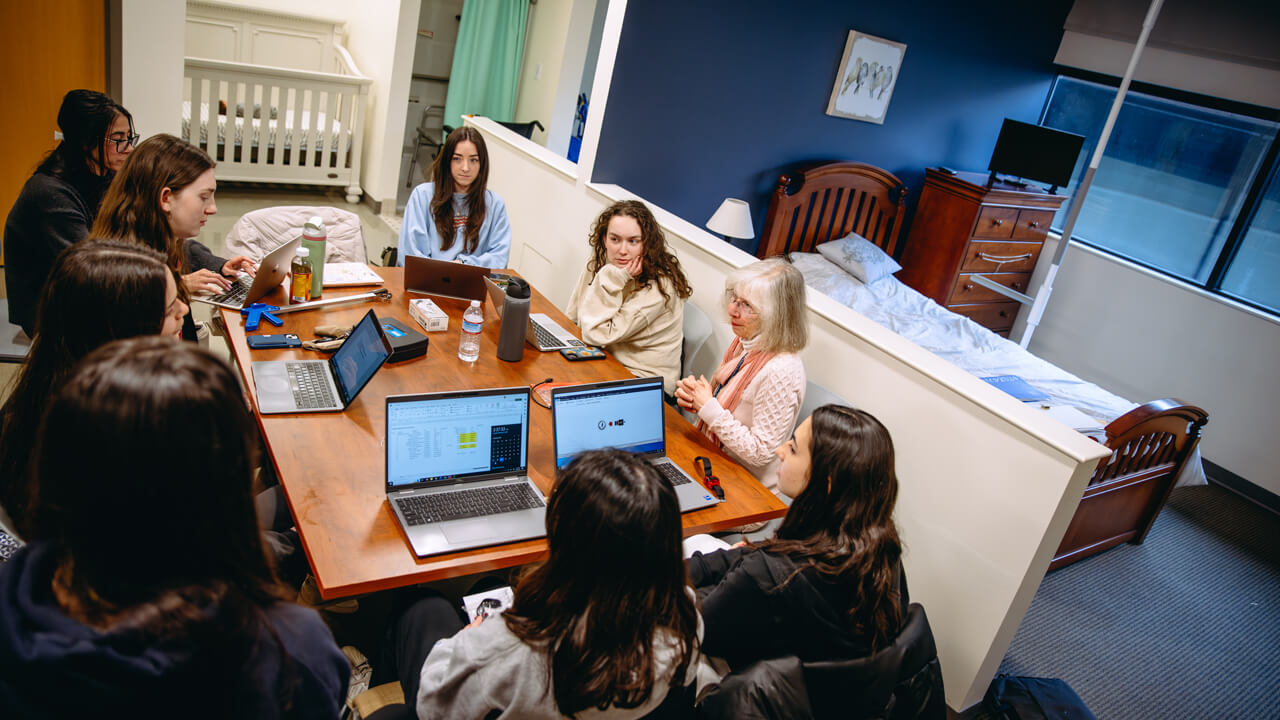 Professor and students sitting around a table in a model apartment