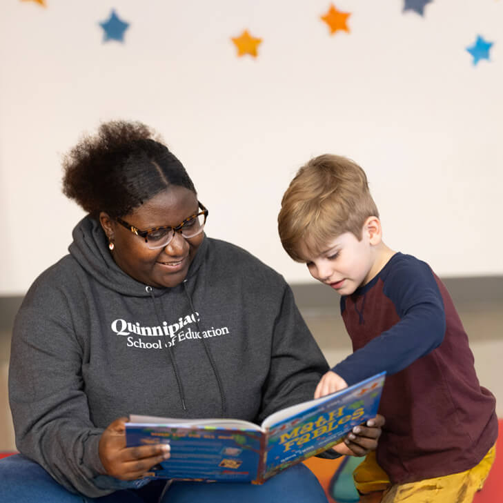 A Quinnipiac education graduate reading a book with a child in a classroom setting.