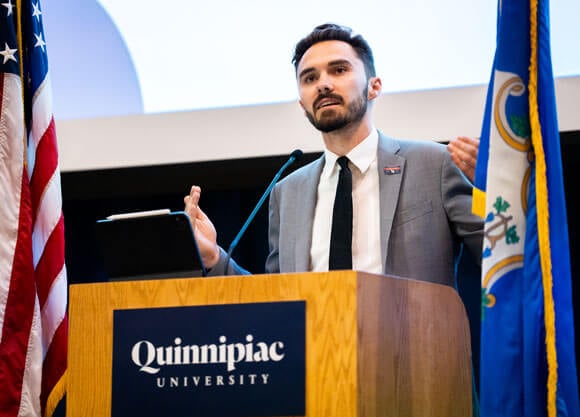 David Hogg stands at a podium and addresses the QU audience