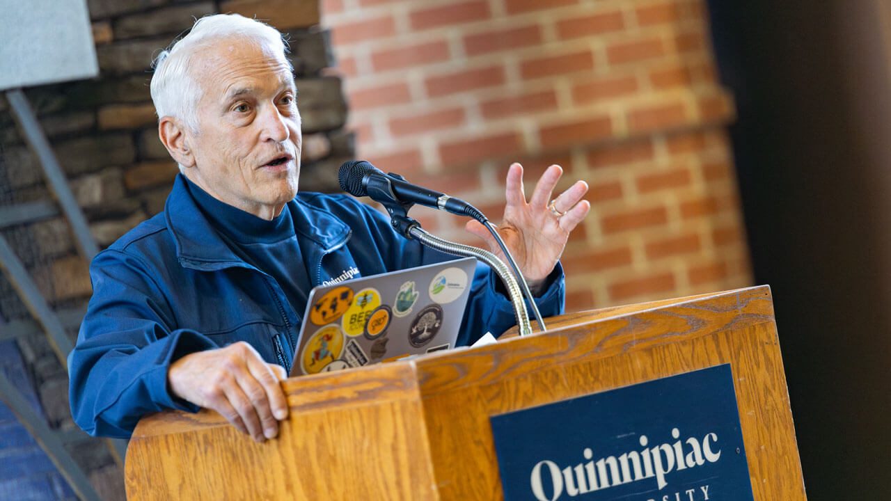 Individual speaking to a crowd at a Quinnipiac podium